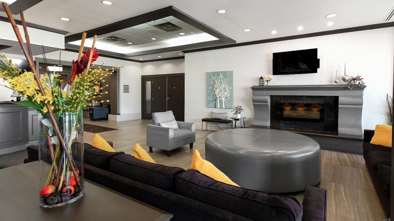 Modern hotel lobby with fireplace, gray seating, yellow accent pillows, and colorful floral arrangement at Coast Calgary University Area Hotel by APA