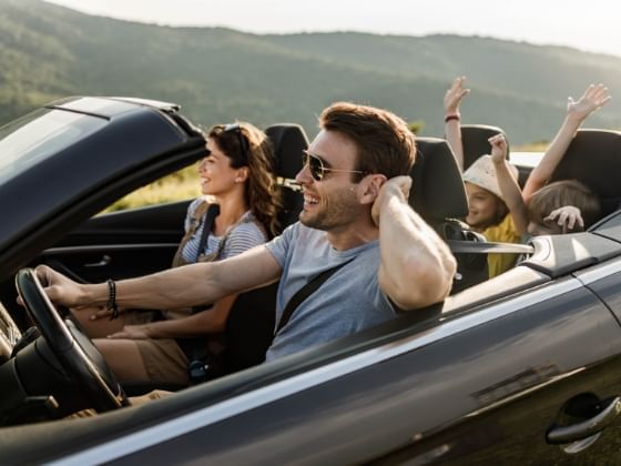 A family rides along a mountainside roadway in a convertible