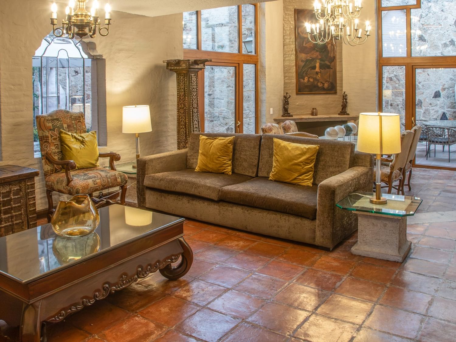 Elegante sala de estar con sofá beige, cojines dorados, candelabros y amplias ventanas en Quinta Real Guadalajara