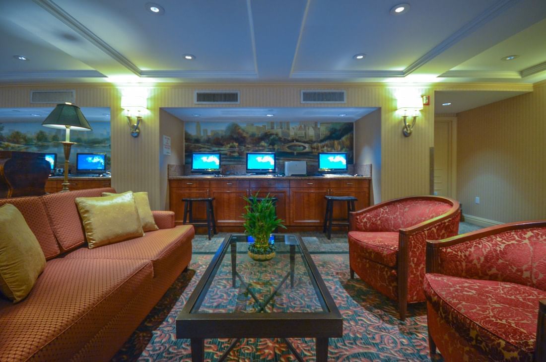 A hotel lobby with a sofa, armchairs, a coffee table, and a bar with TVs.