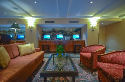 Hotel business lounge with a red couch, glass table, two armchairs, and three computers behind a counter.