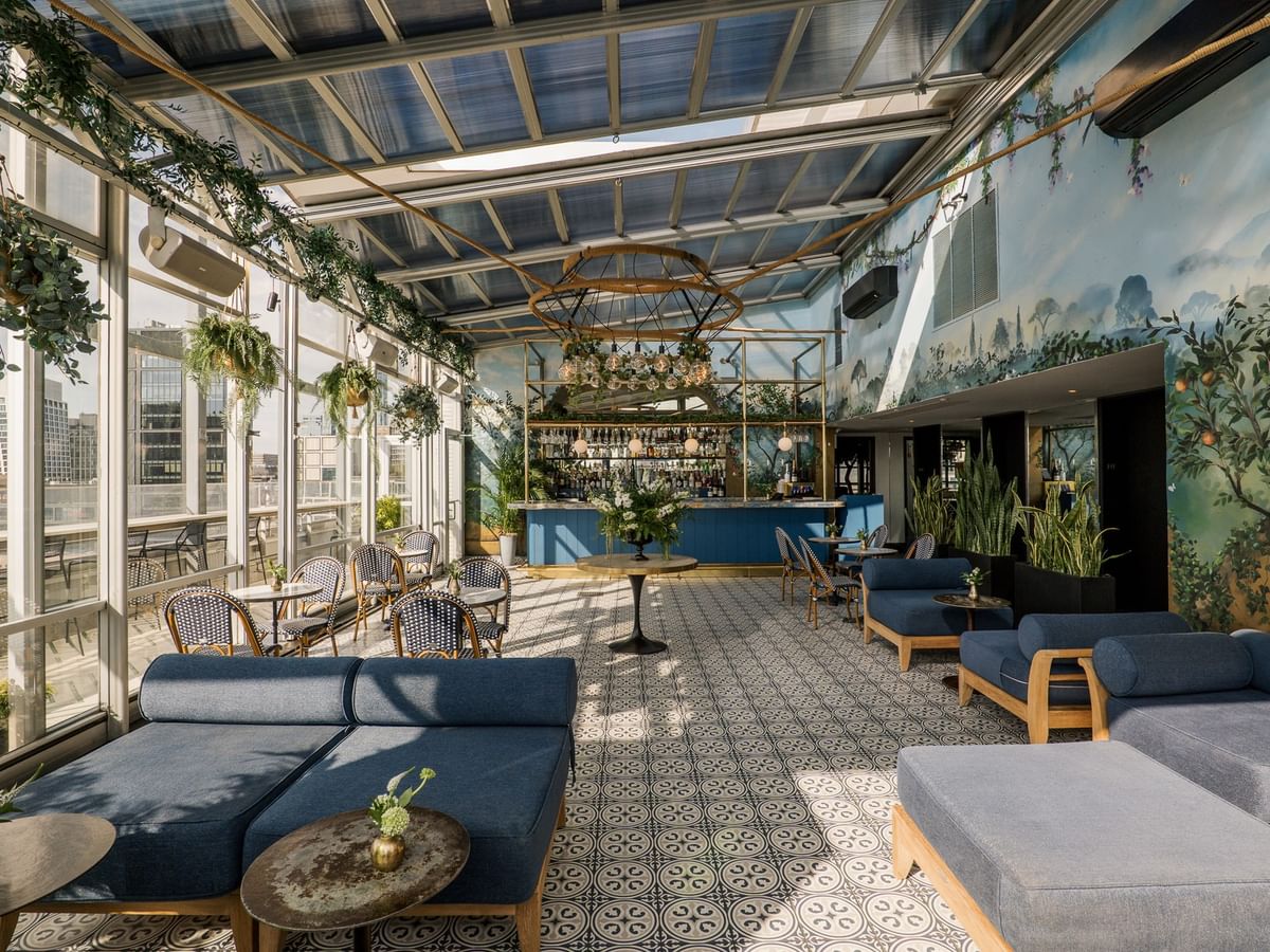 Eden at Gansevoort Rooftop features botanical murals, blue lounge seating, and a bar under a glass ceiling in New York.
