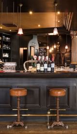 Wine bottles displayed behind a counter with leather bar stools and hanging lights at The Chutney\’s Restaurant