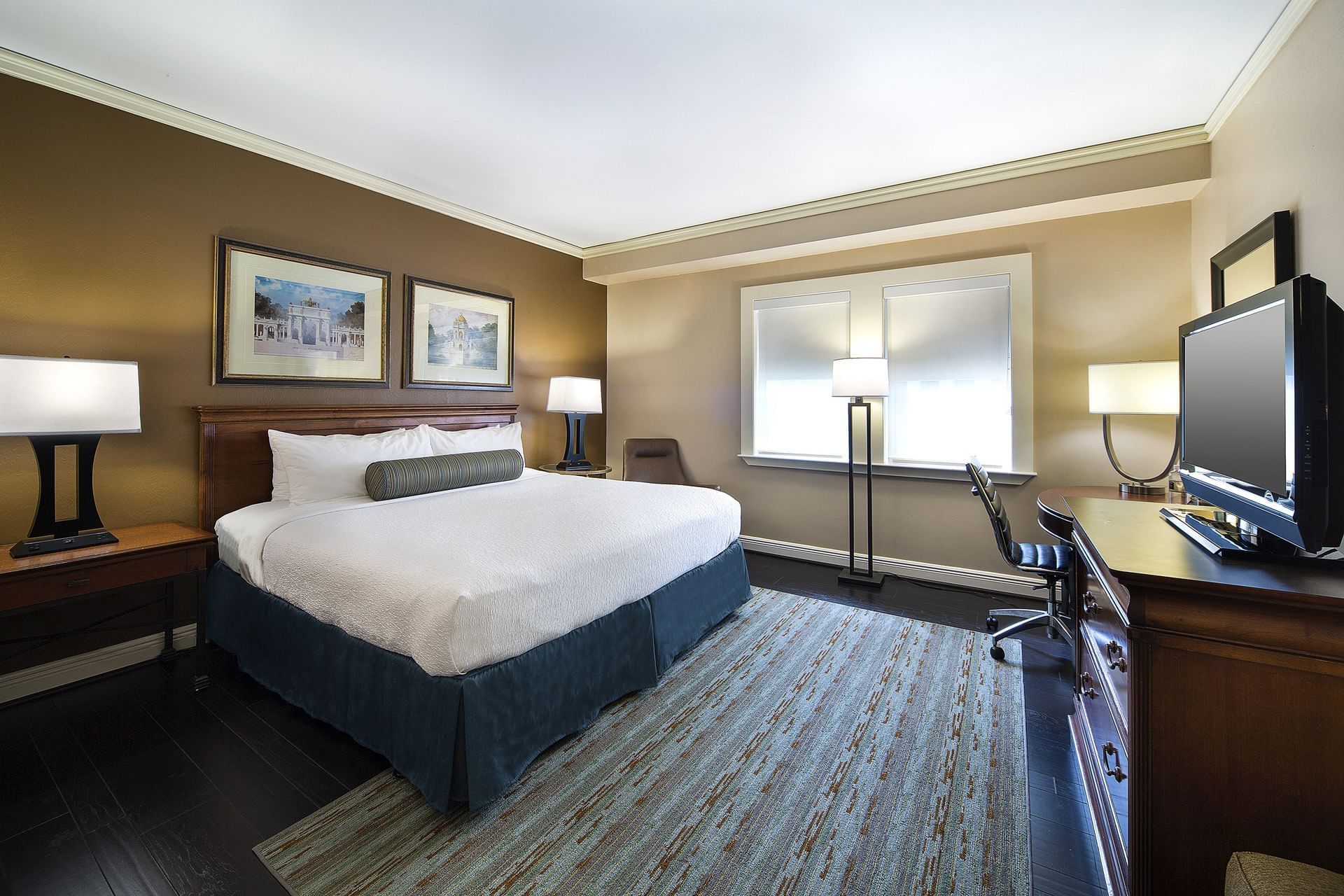 A hotel room with a bed, two lamps, a window, a chair, and a rug.