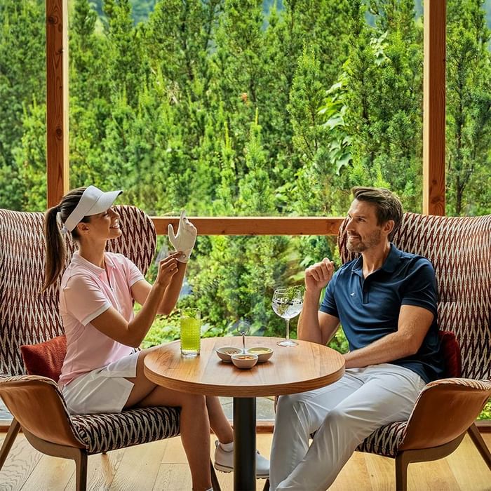 Golferpaar genießt Drinks auf Terrasse mit Waldblick bei Falkensteiner Group