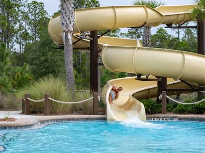 Golden water slide spiraling into a sparkling pool surrounded by lush palms and greenery at Camp Creek Inn in Inlet Beach.