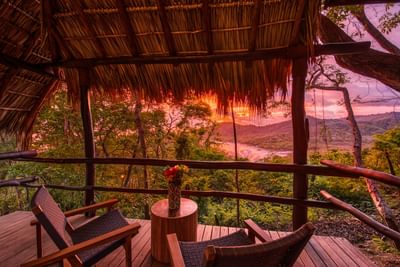 Sillas de madera en la terraza de los bungalós con vistas al mar durante una puesta de sol rosada en Morgan's Rock, lugares ideales para alojarse en Nicaragua.