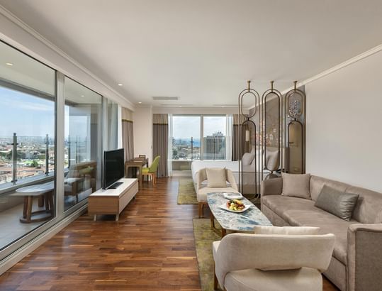 Titanic Port Bakırköy'de, şehir manzarasına bakan büyük pencerelere sahip; kanepe, sehpa ve TV ile donatılmış Junior suite odada modern oturma alanı.
