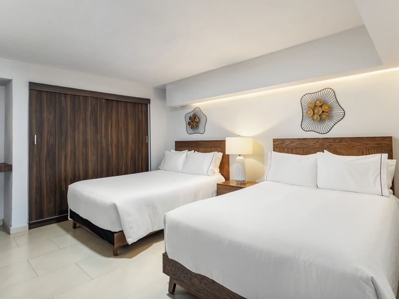 Junior Suite Vista Parcial Al Mar with two white-linen beds, decorative wall art, and a dark wood door at Sunvivia Mazatlán