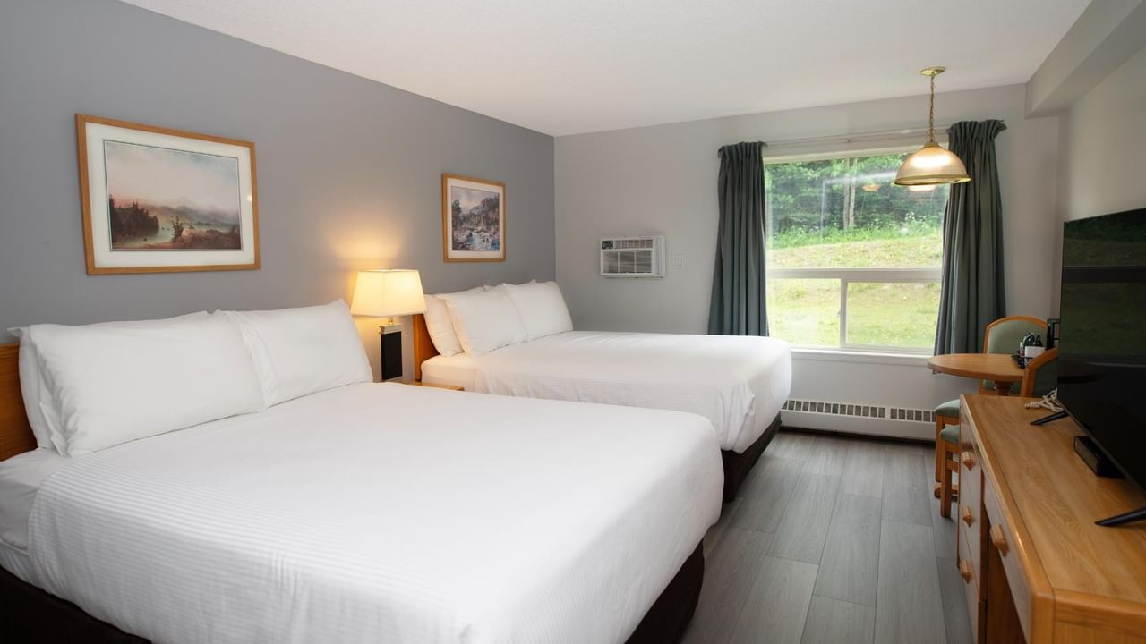 Two beds, nightstands, a window, two framed paintings, a TV, and a table with a chair.