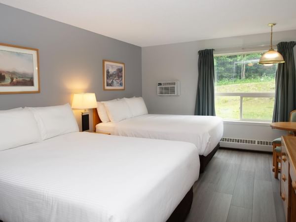 Hotel room with two beds, a table with a TV, and framed art on the wall.