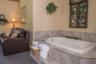 Jetted tub beside a brown leather couch with robes placed on the step in Tuscany Themed Suite at Hilltop Inn, Salmon Arm