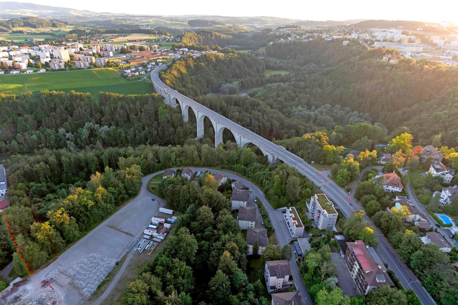 Aerial view of the St. Gallen Bridge surrounded by a dense forest and urban areas near Hotel des Innovations