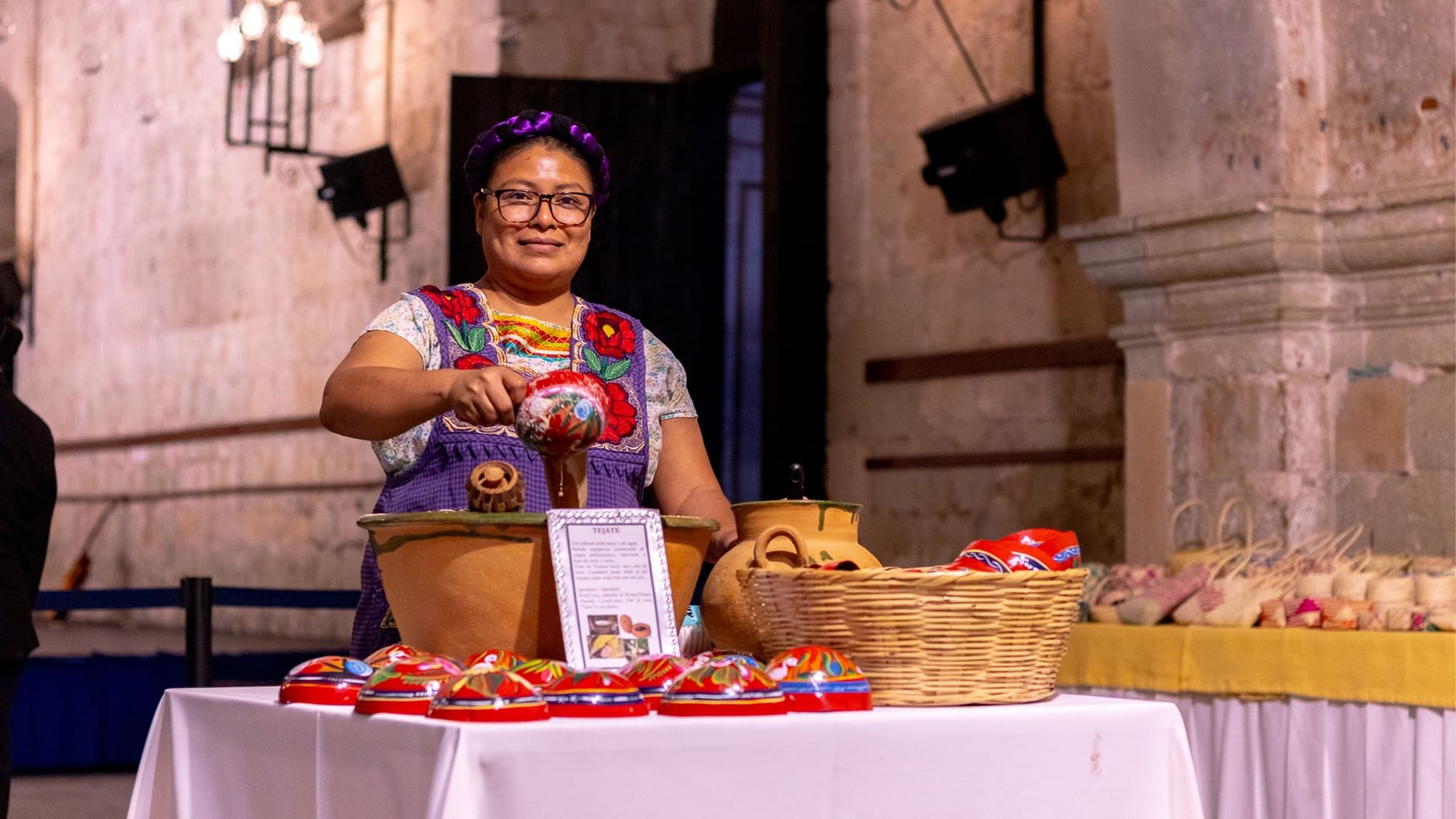 A woman in traditional dress serving a dark drink from a large clay bowl at Quinta Real Oaxaca