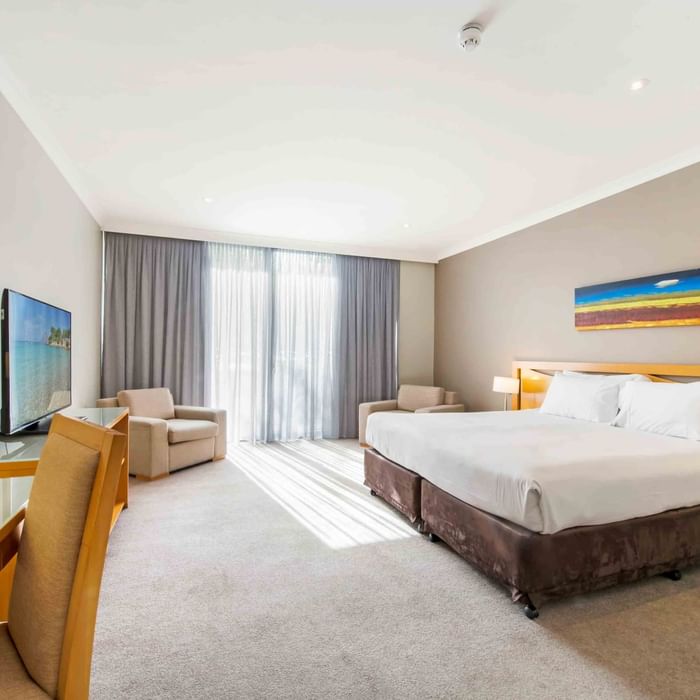 Standard Room with a King bed, armchairs, TV, and sunlit curtains at Mercure Kooindah Waters