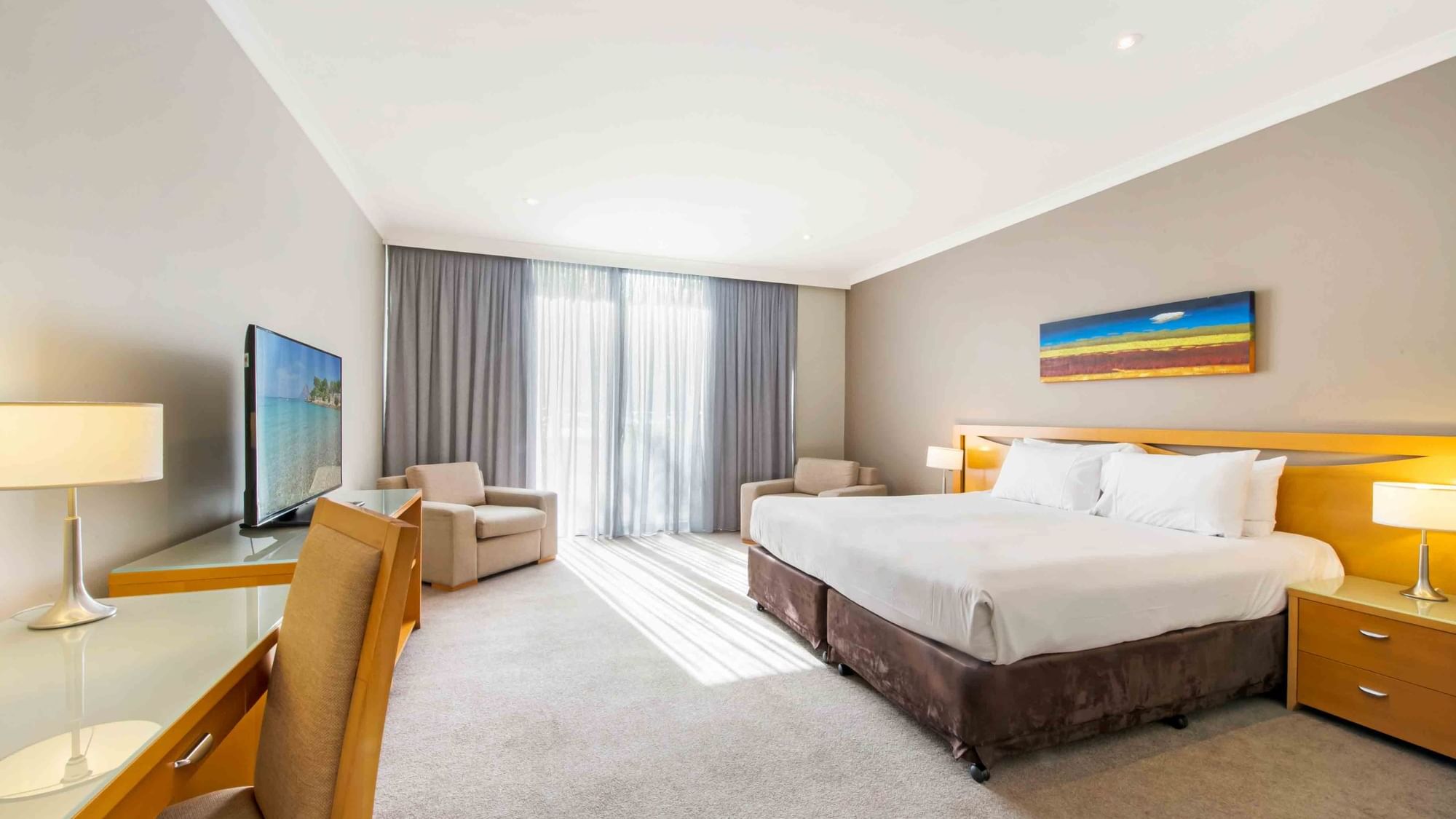 Standard Room with a King bed, armchairs, TV, and sunlit curtains at Mercure Kooindah Waters