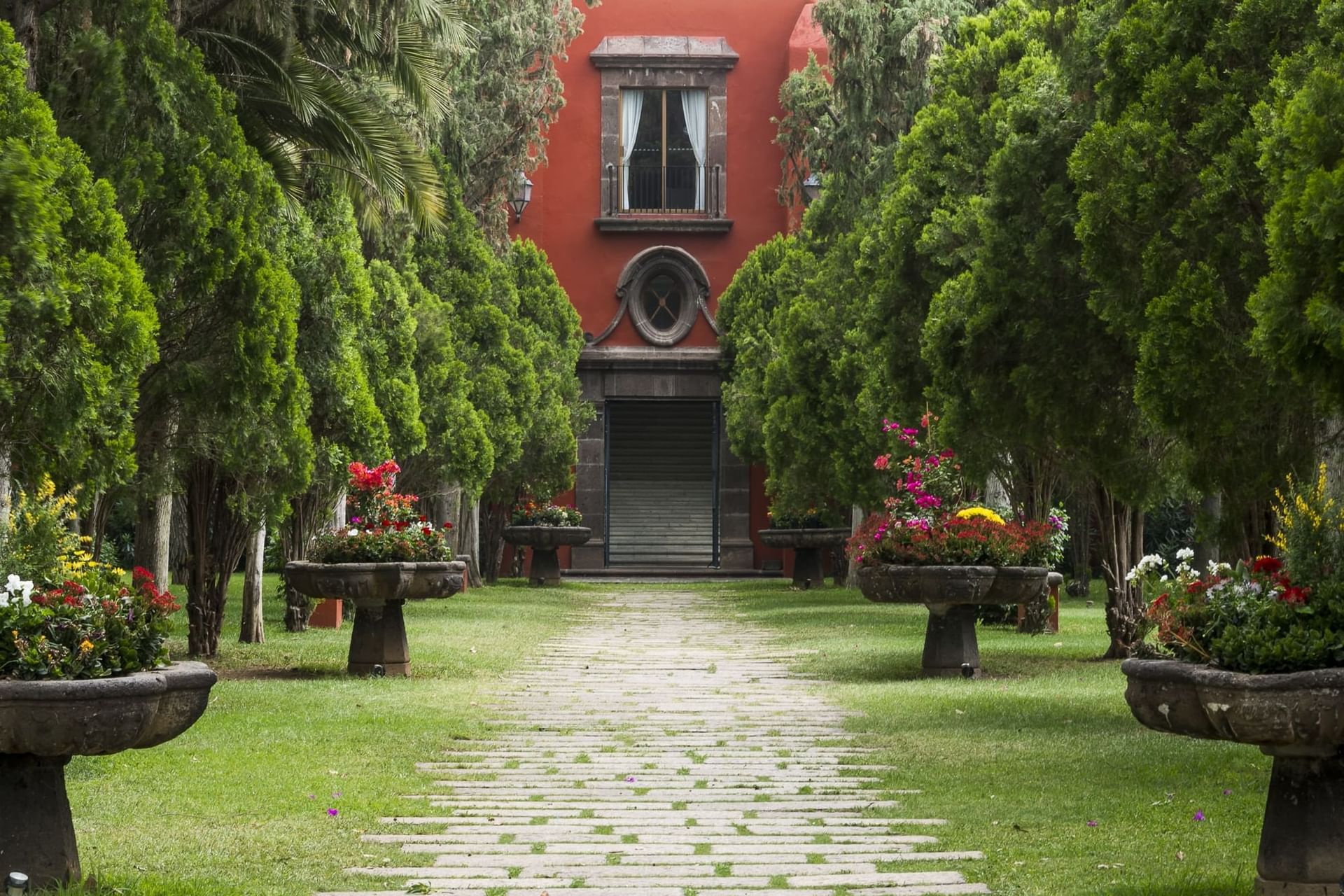 Cobblestone pathway leading to a Fiesta Americana Hacienda Galindo Resort & Spa flanked by green trees and flowerpots