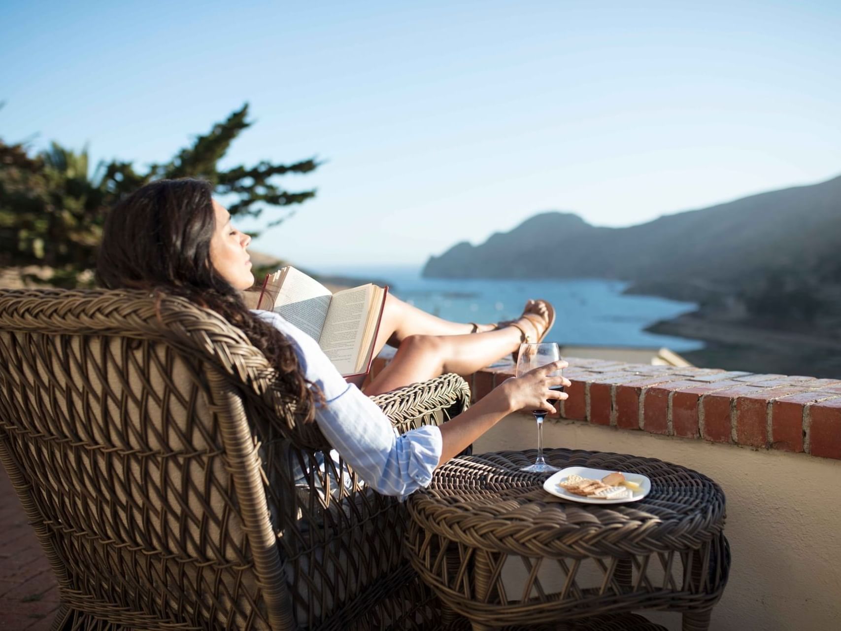 Lady relaxing in a wicker chair with a glass of wine in Ocean View Queen with Two Twins at Banning House Lodge