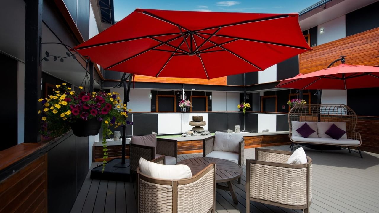 Outdoor lounge with wicker chairs, red umbrellas and potted plants on a wooden deck.