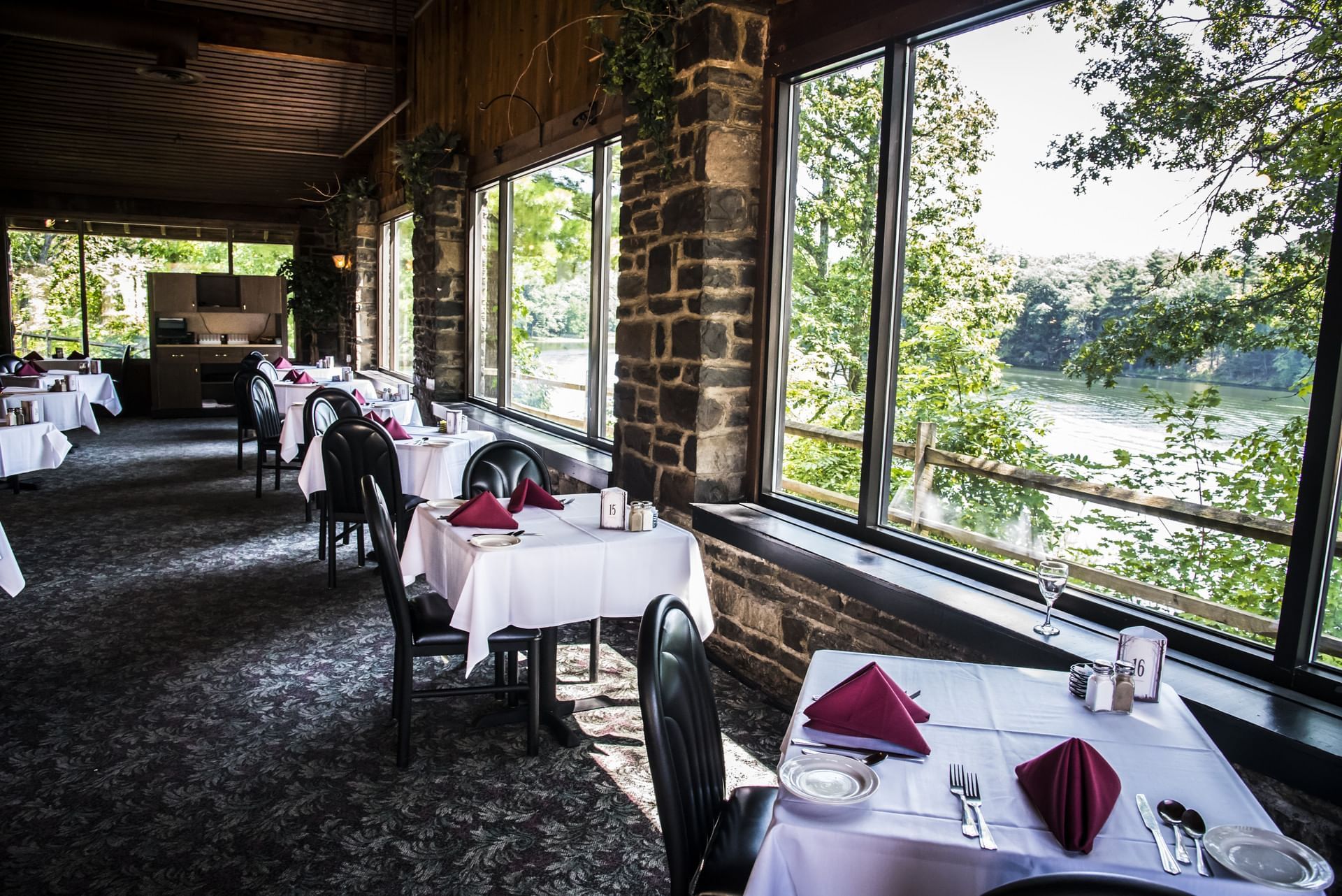 Cozy restaurant with stone walls, white tablecloths, and large windows overlooking a tranquil river at Cove Pocono Resorts