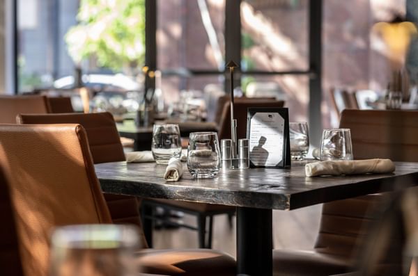 Elegant table with glassware by leather chairs under warm light in Gattara Restaurant & Patio at Warwick Denver