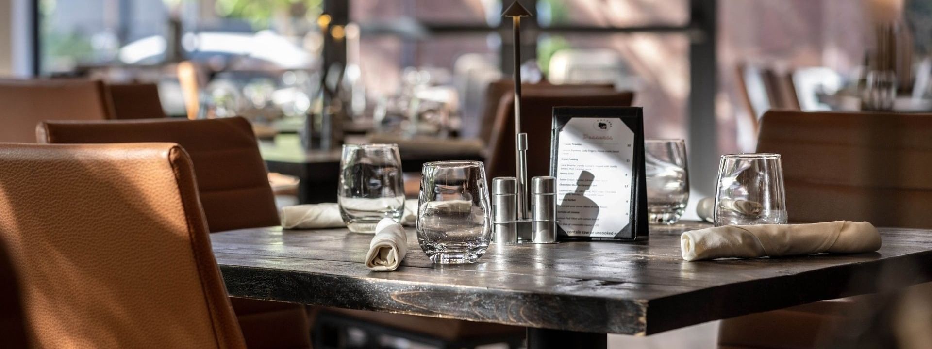 Elegant table with glassware by leather chairs under warm light in Gattara Restaurant & Patio at Warwick Denver