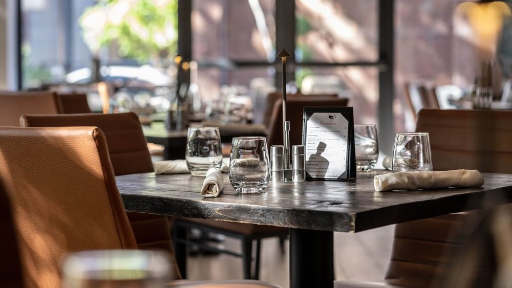 Elegant table with glassware by leather chairs under warm light in Gattara Restaurant & Patio at Warwick Denver