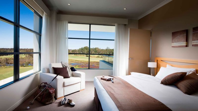 Room with a bed, adjacent sitting area, golf equipment, and a view of a field through the window at Mercure Kooindah Waters