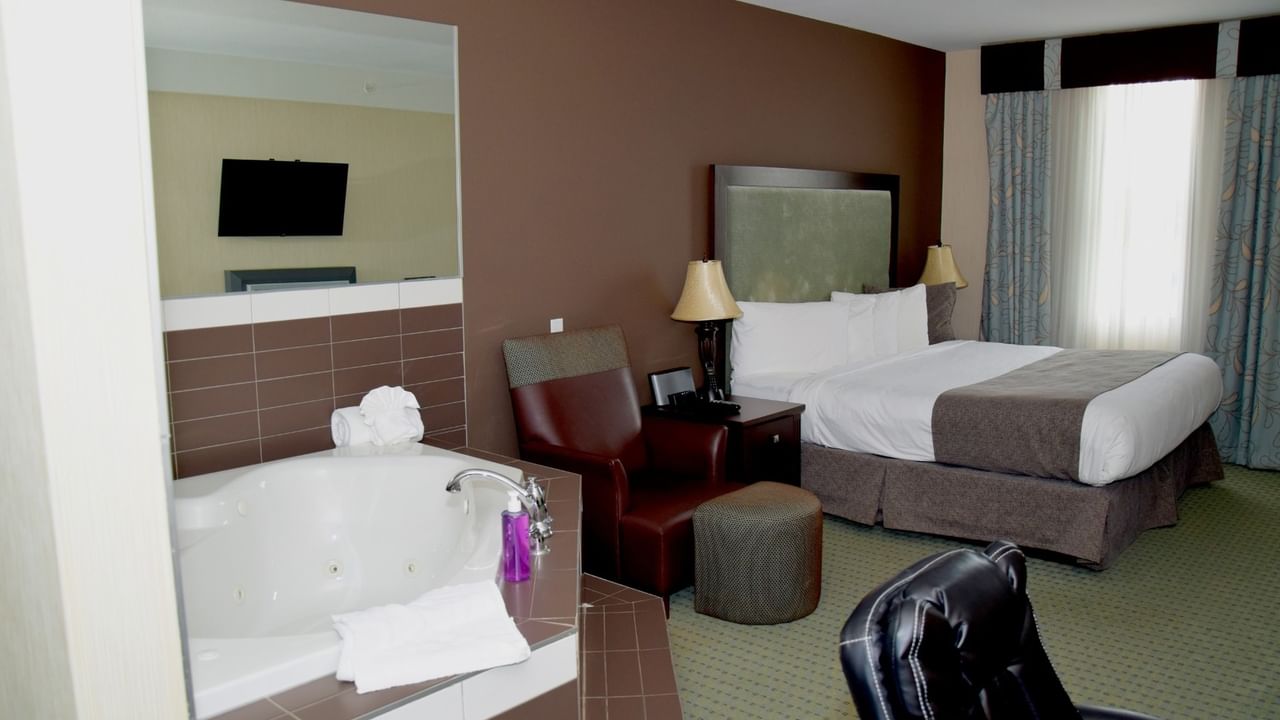 Hotel room with large bed, jetted tub, armchair, desk, and window with curtains.