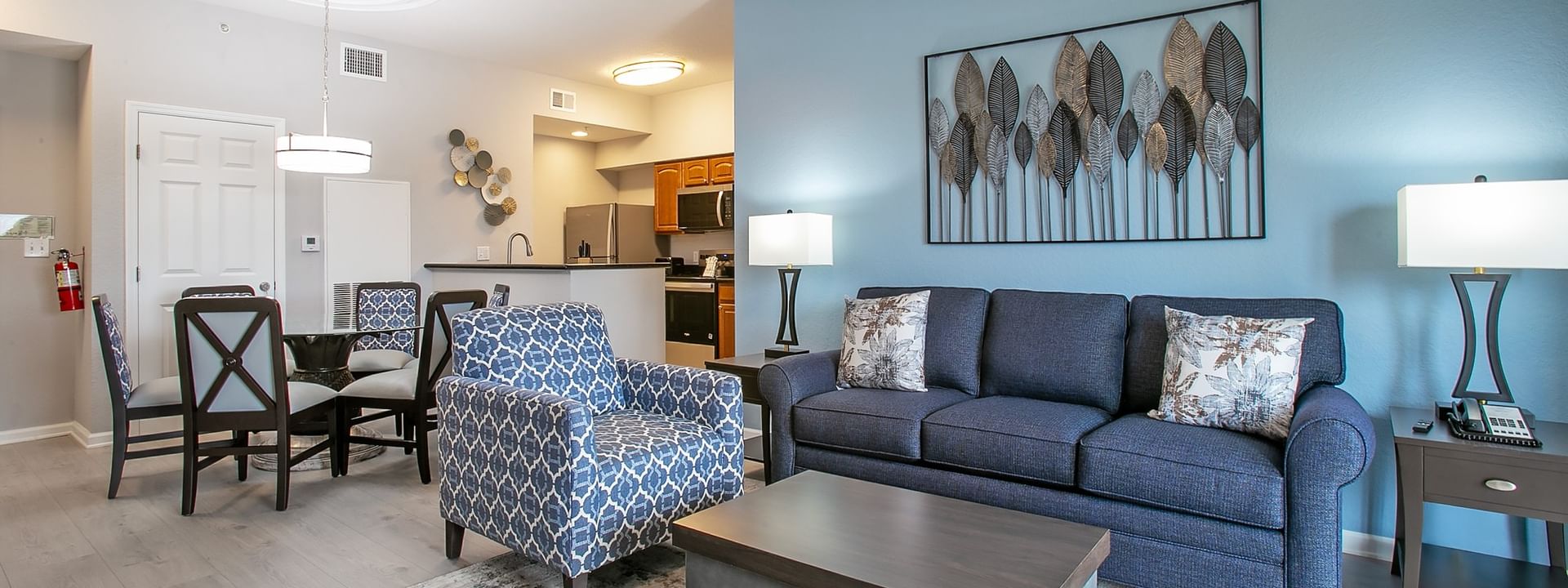 A spacious living area with a sofa, armchair, coffee table, dining table, and kitchenette.