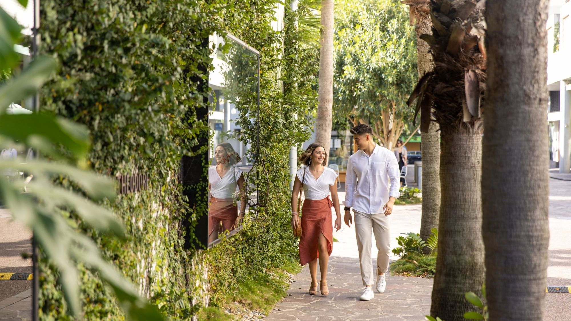 Couple walking on James Street next to a green wall near Sofitel Brisbane Central
