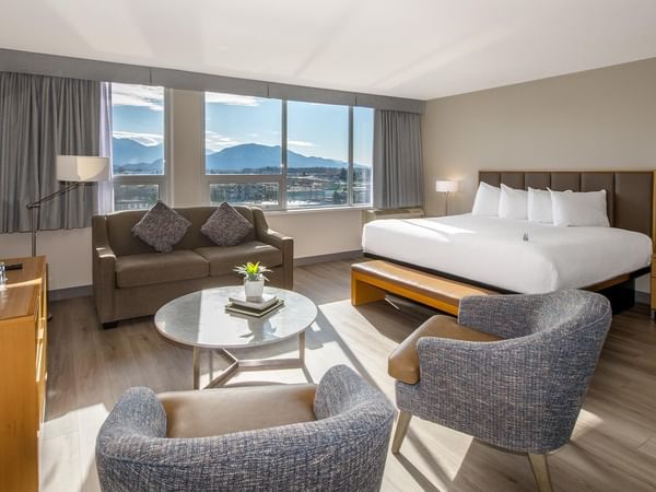 A large hotel room with a king bed, sofa bed, and lounge chairs.