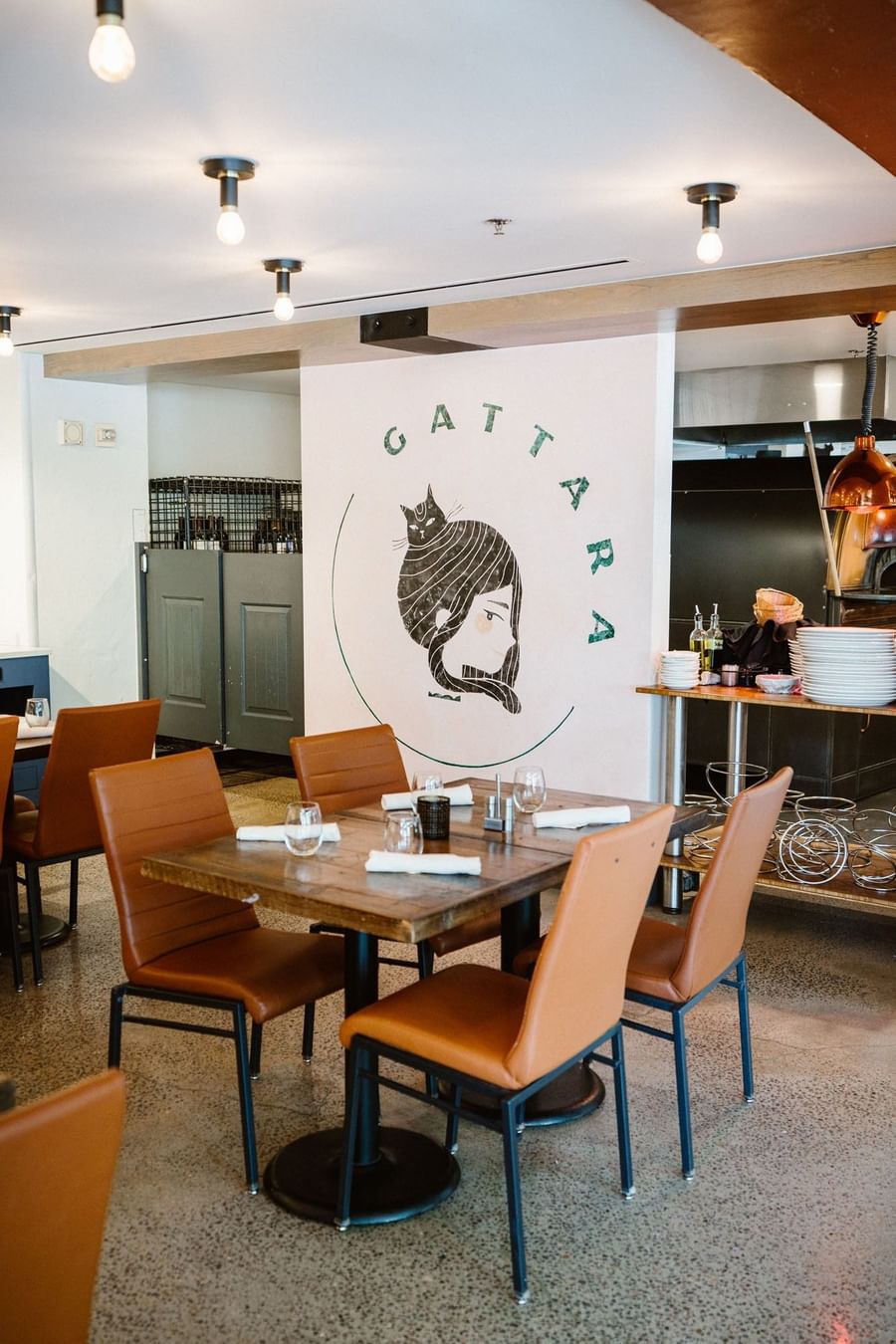 Gattara restaurant interior with cat logo on wall near tables, brown chairs, and kitchen at Warwick Denver