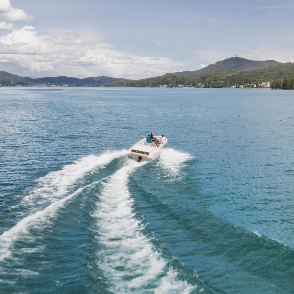 Motorboot fährt mit hoher Geschwindigkeit über das türkisblaue Wasser des Wörthersees mit bewaldeten Bergen im Hintergrund