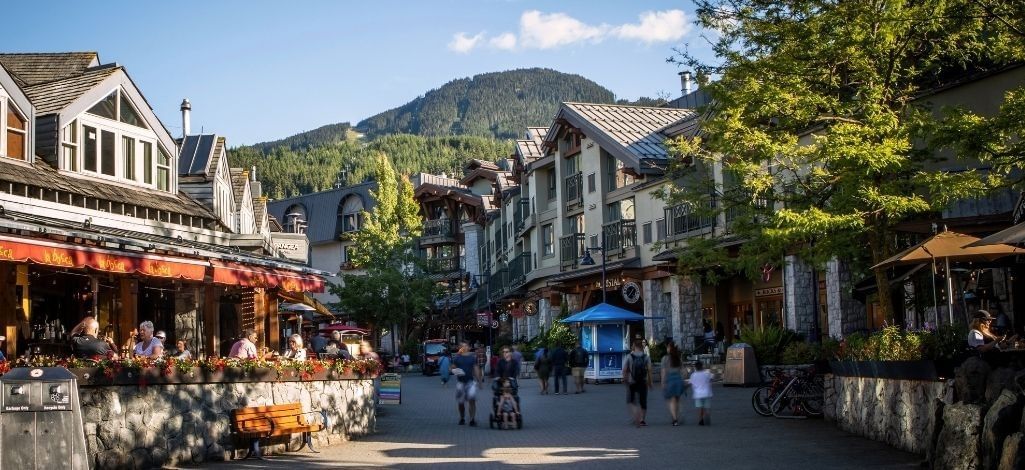Pedestrians explore shops and restaurants along a sunny street in Whistler Village.