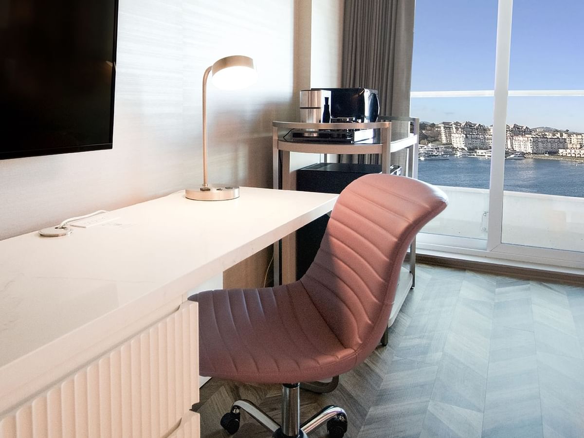 Hotel guestroom with TV, chair, work desk, coffee machine, and an ocean view.