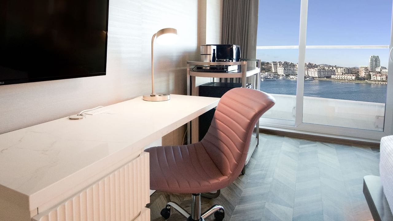 Hotel guestroom with TV, chair, work desk, coffee machine, and an ocean view.