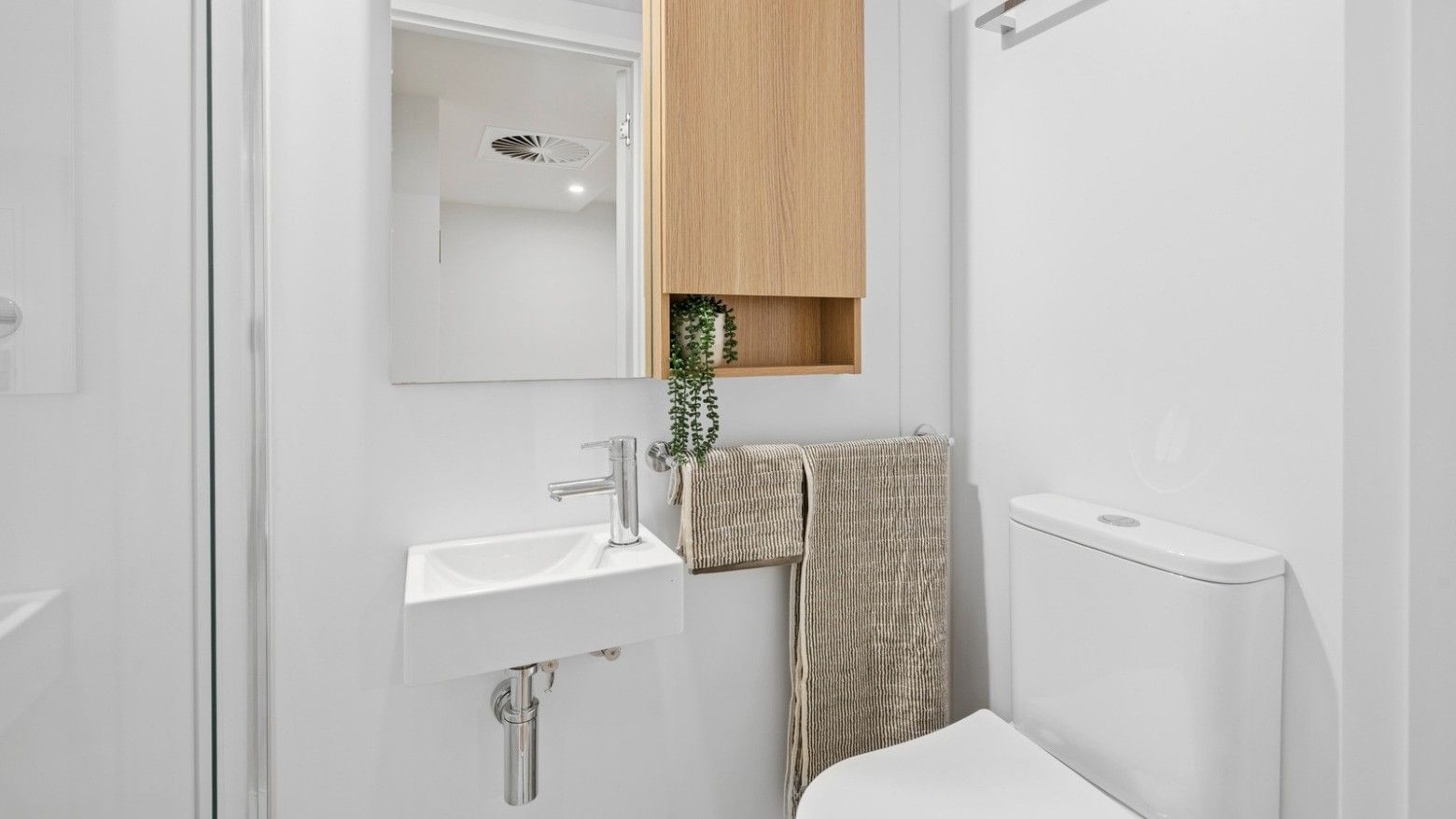 Modern bathroom with white toilet, sink, and wooden cabinet at UniLodge Brisbane City.