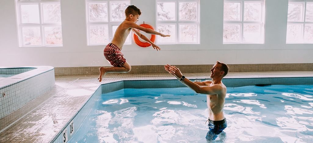 father catches his son who is jumping into a pool