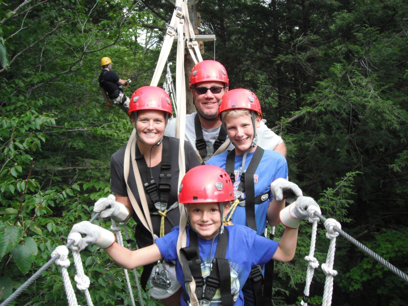 Family of four with red helmets on a suspension bridge, smiling for the camera.