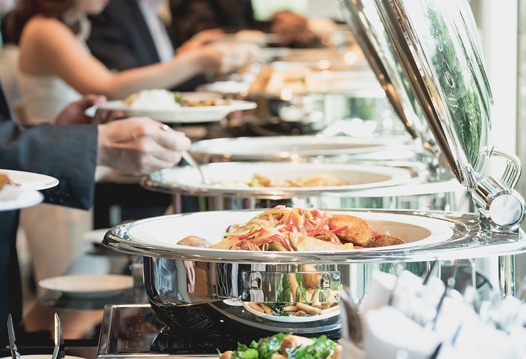 hands grabbing food from silver buffet servers