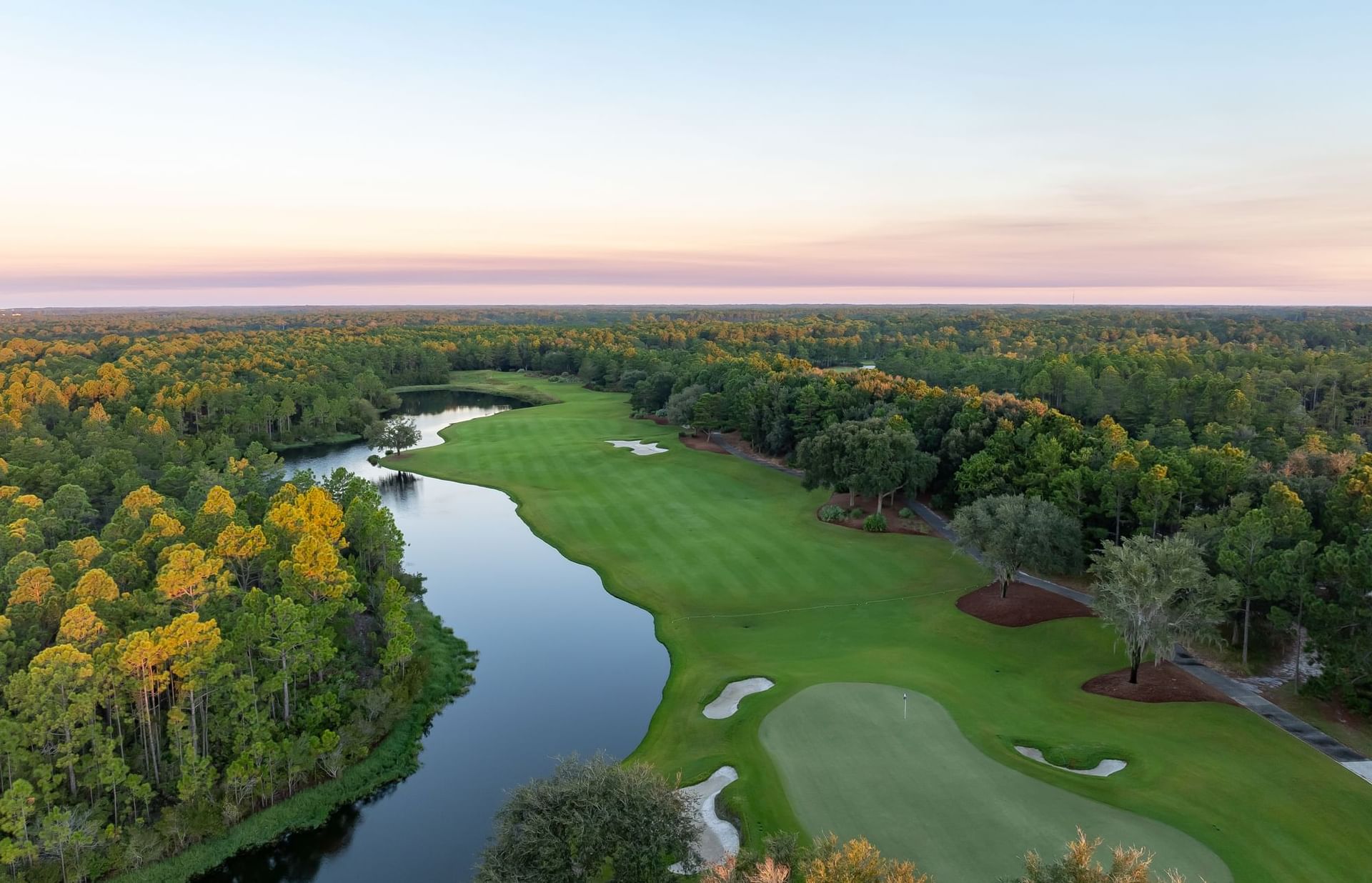 Aerial view of a golf course with a river running through it and a sunset sky.