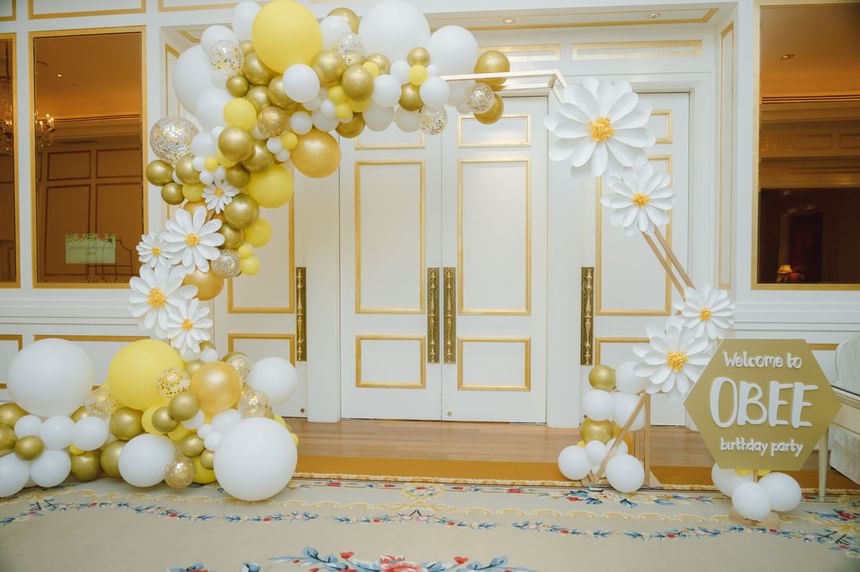 OBEE birthday party entrance decorated with gold and white balloons and large flowers at Park Hyatt Saigon