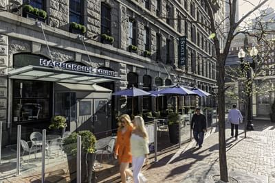 People walking on a brick sidewalk past the Harborside Lounge entrance with outdoor seating in Harborside Inn Boston