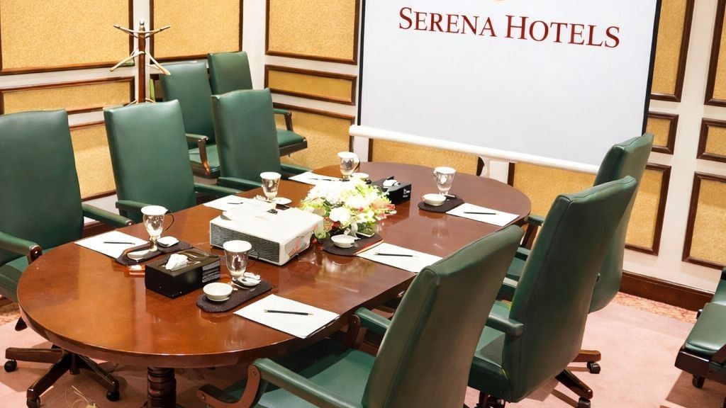 Sleek office chairs lined at a long wooden table with a large wall monitor at Serena Hotels & Resorts