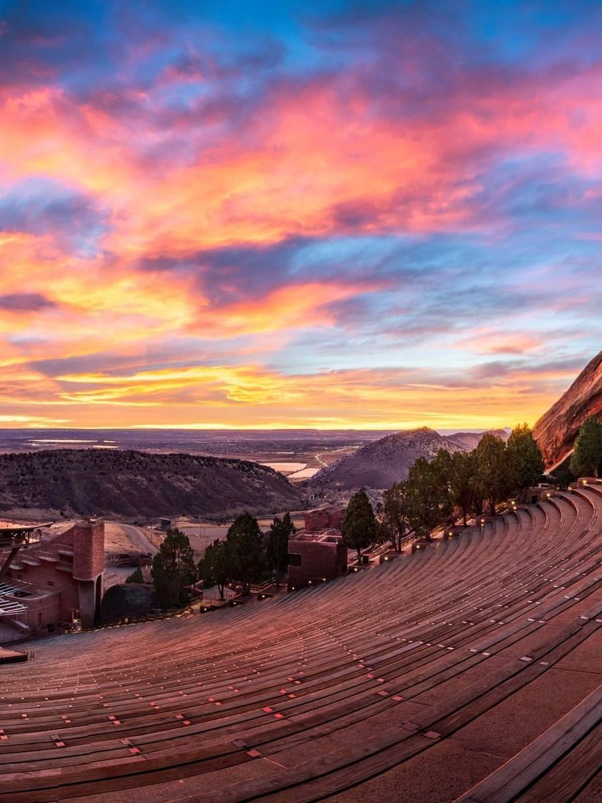 Red Rocks Amphitheatre with Stone benches by a rock formation under a vibrant sunset at an arena near Warwick Denver