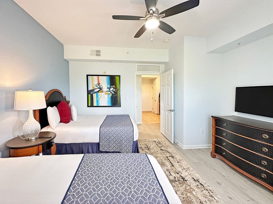 A wide view of a hotel suite with two beds, a dresser, and a TV