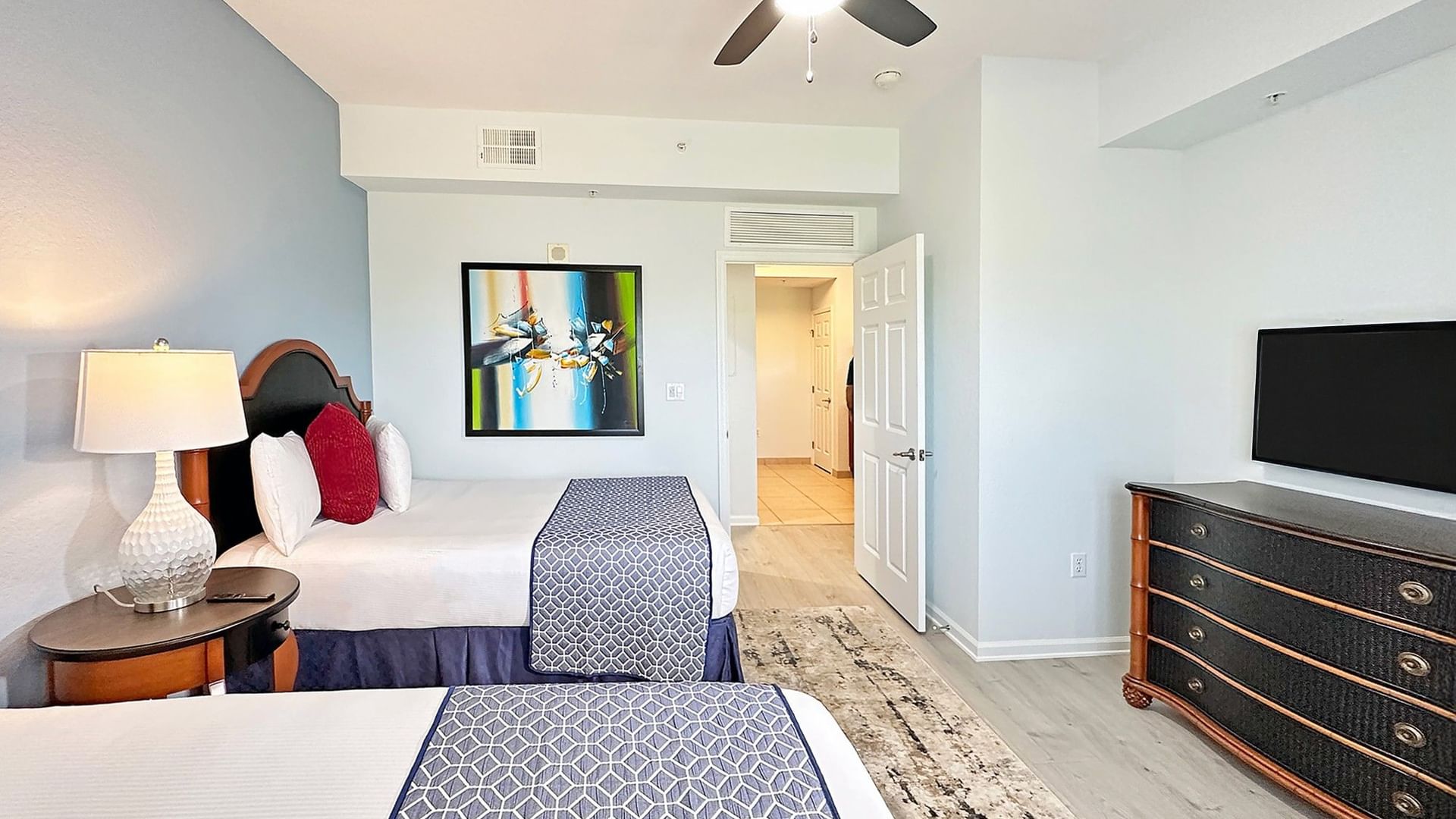 A wide view of a hotel suite with two beds, a TV, and a dresser.