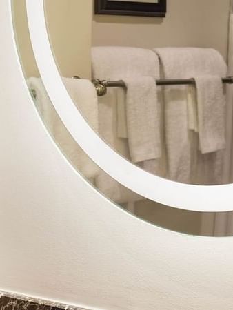 Round backlit mirror by plush white towels on a metal rack near a vanity in Twin Room at Warwick San Francisco
