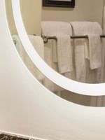 Round backlit mirror by plush white towels on a metal rack near a vanity in Twin Room at Warwick San Francisco